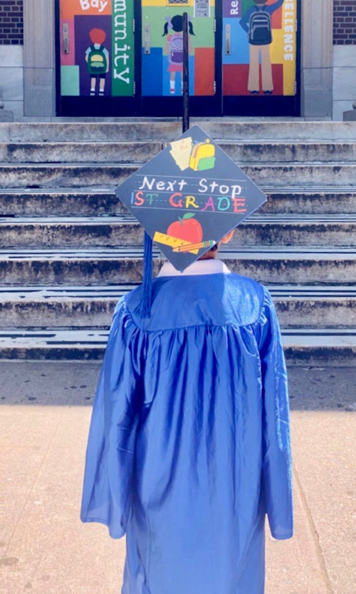 Child in blue gown wearing Next Stop 1st Grade cap on steps