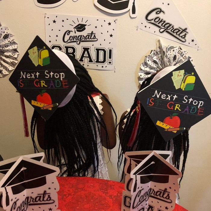 Two girls wearing Next Stop 1st Grade caps at backdrop