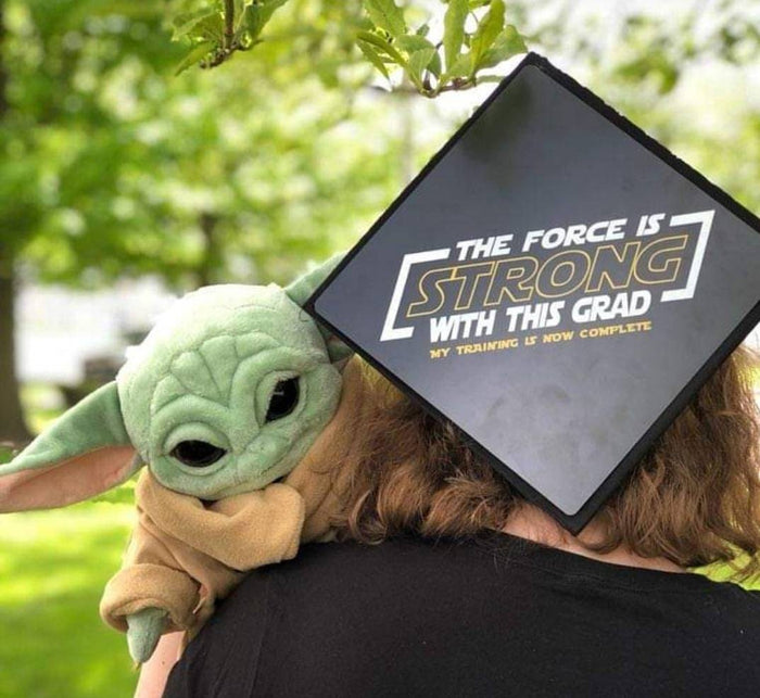 Person wearing Force Is Strong cap hugging Baby Yoda plush