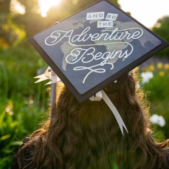 Graduate wearing And So The Adventure Begins cap