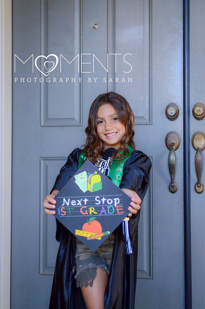 Young girl in gown holding Next Stop 1st Grade cap