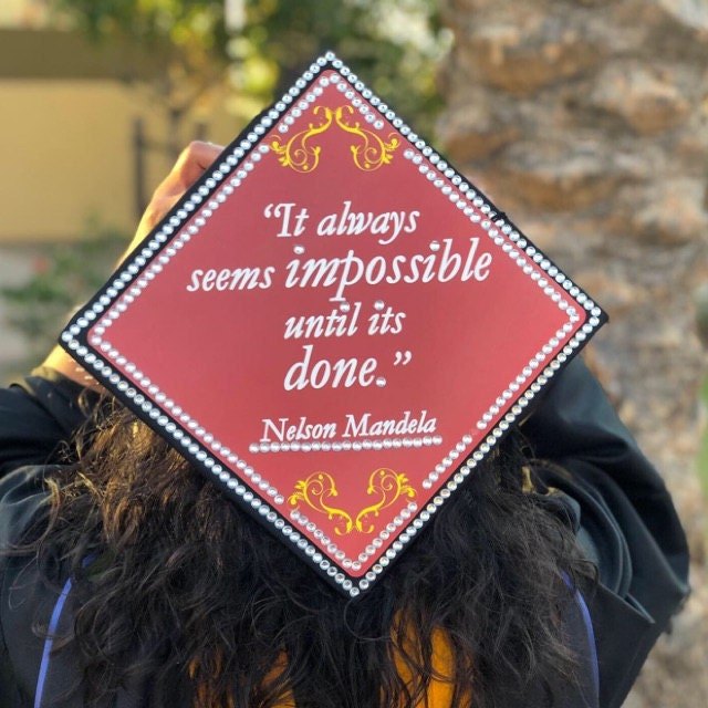 Graduate holding Mandela Impossible Until Done cap