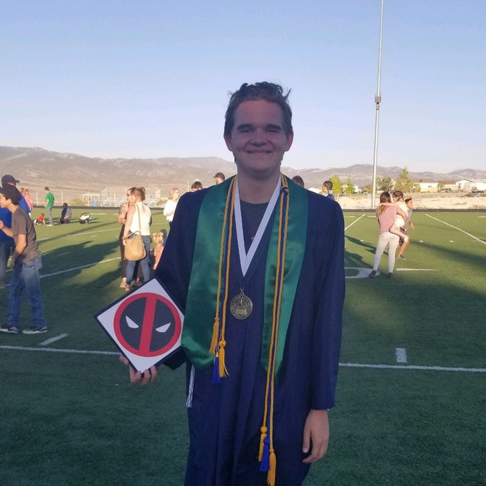 Graduate holding Deadpool logo cap on field