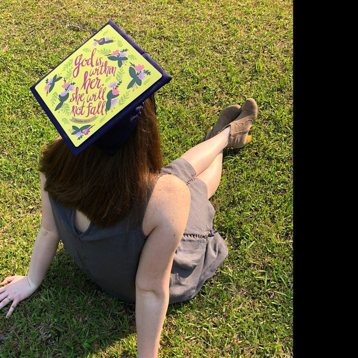 Woman wearing hummingbird God Is Within Her cap on grass