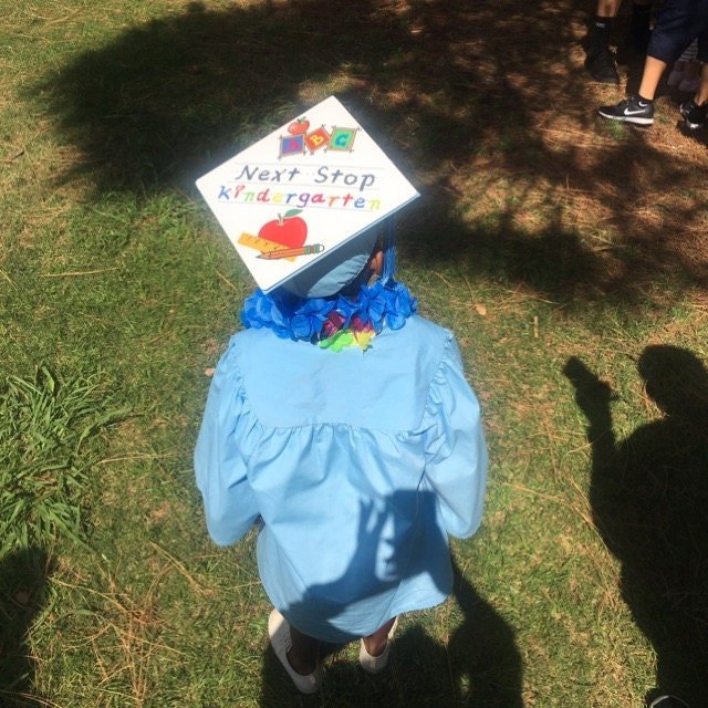 Child in blue gown wearing Next Stop Kindergarten cap