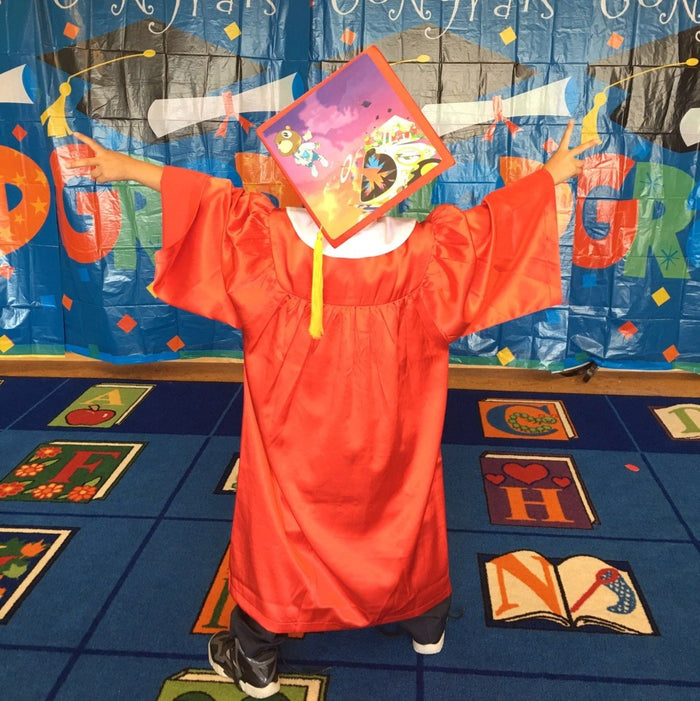 Child in red gown wearing Kanye cap in classroom