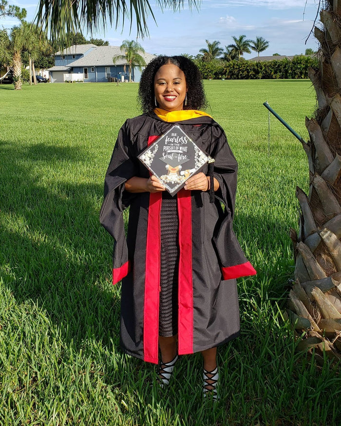 Graduate in doctoral gown holding Be Fearless cap on lawn