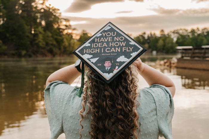 Woman holding Michael Scott How High I Can Fly cap by lake