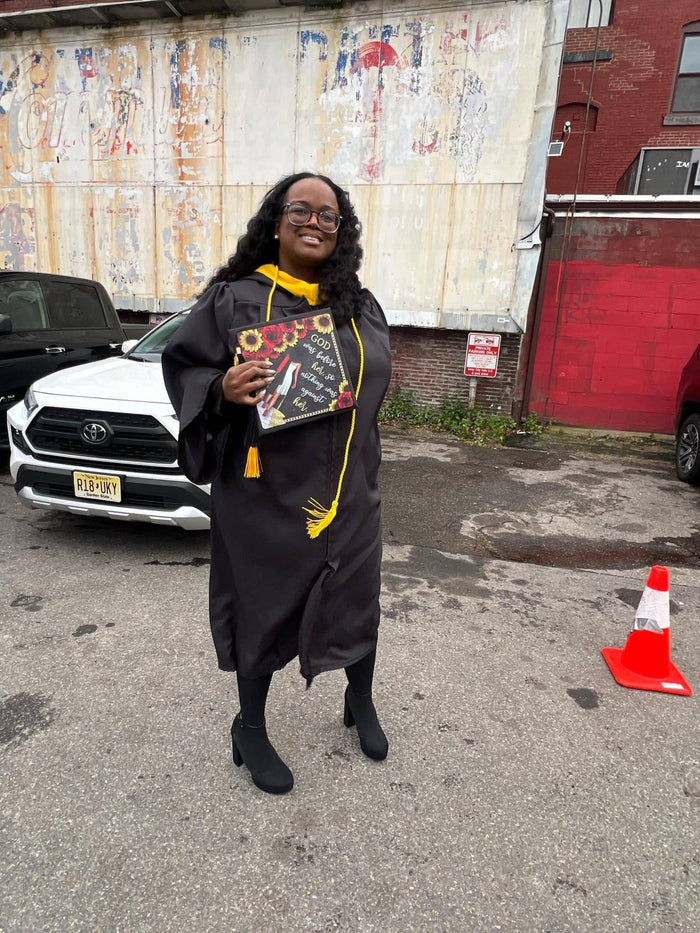 Graduate holding God Was Before Her sunflower cap