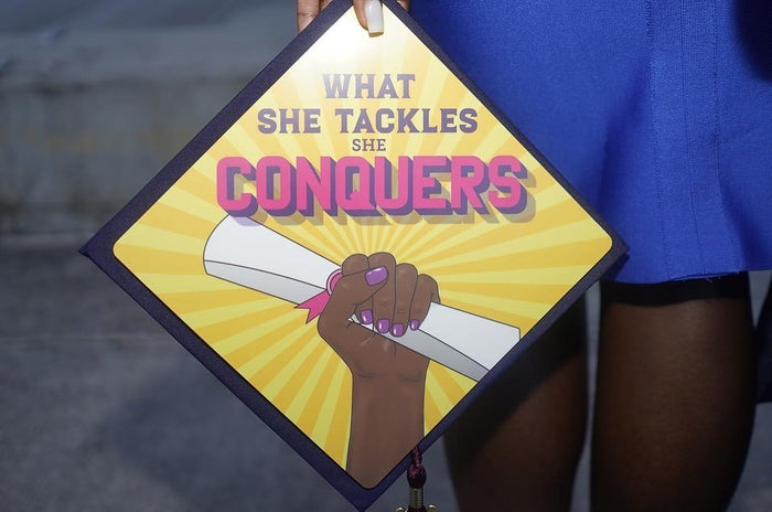 Person holding What She Tackles She Conquers topper