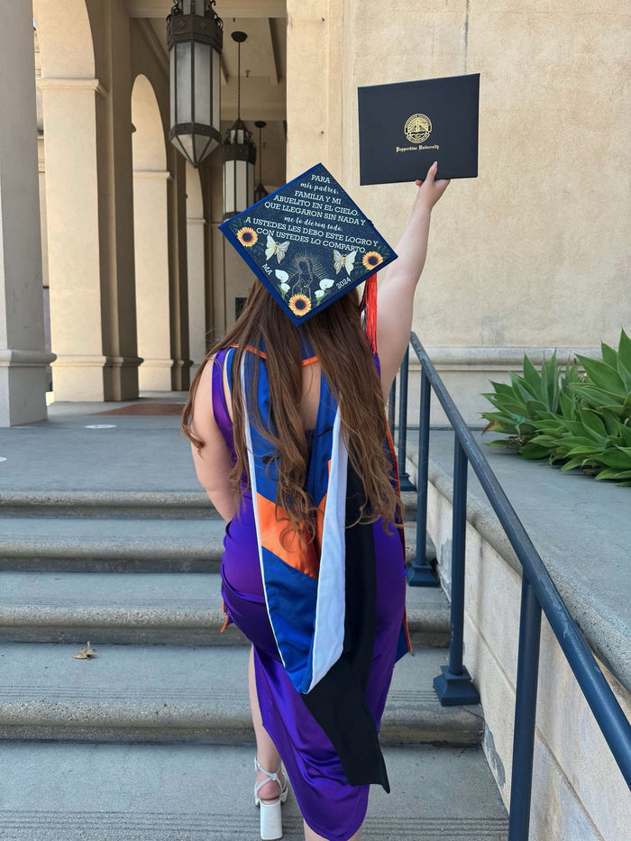 Graduate wearing decorated cap holding diploma on steps