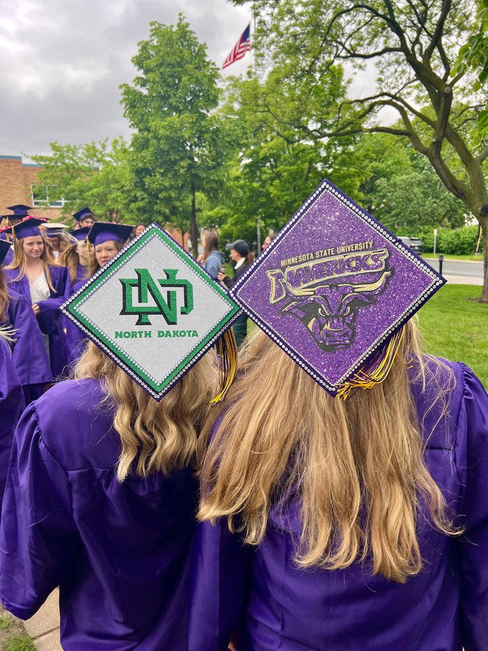 Two graduates wearing North Dakota and Mavericks caps