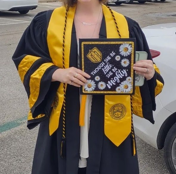 Doctoral graduate holding Though She Be Little cap