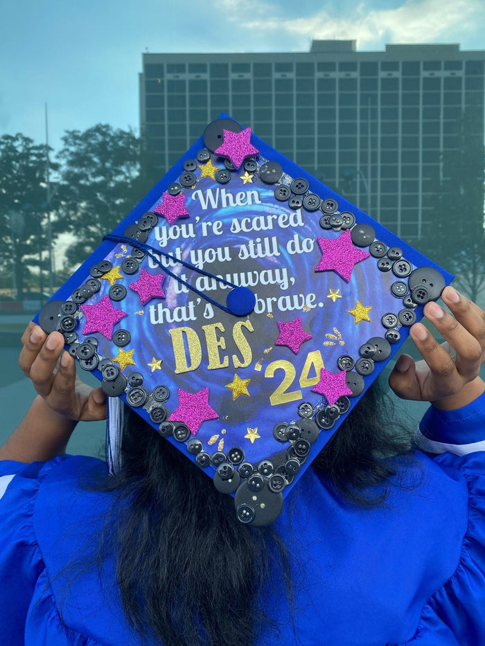 Graduate holding When Youre Scared Brave DES cap over head
