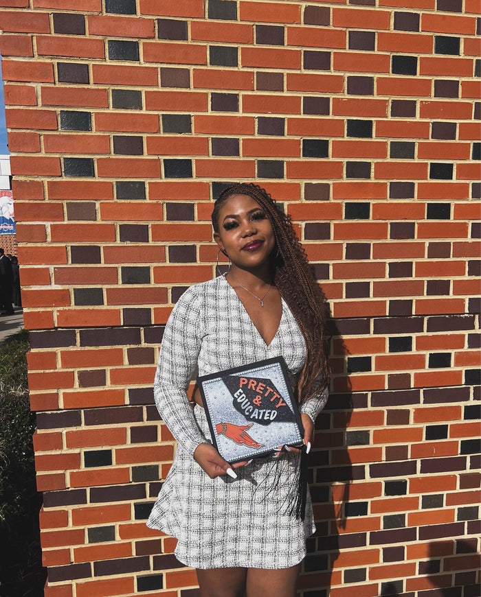 Woman holding Pretty Educated topper at brick wall