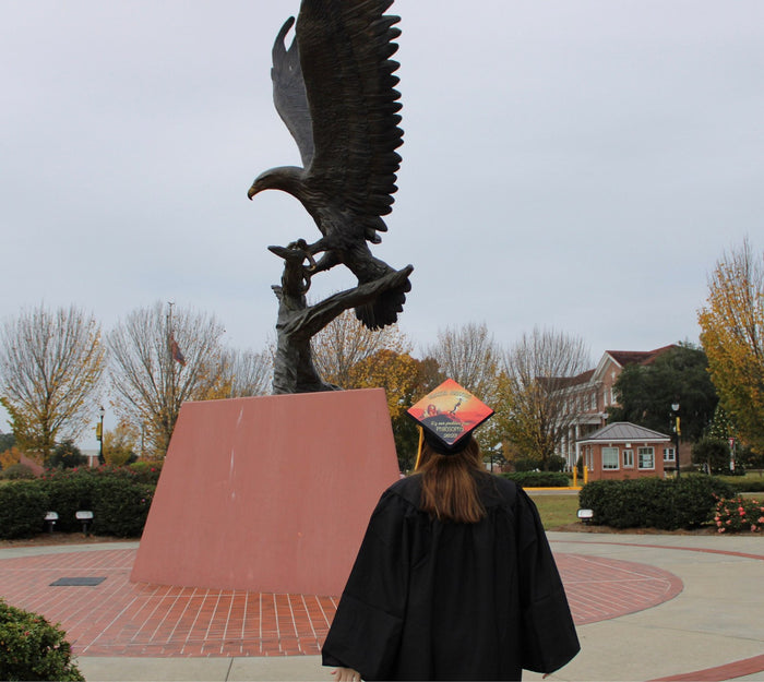 Graduate wearing Hakuna Matata Philosophy 2023 cap at eagle statue