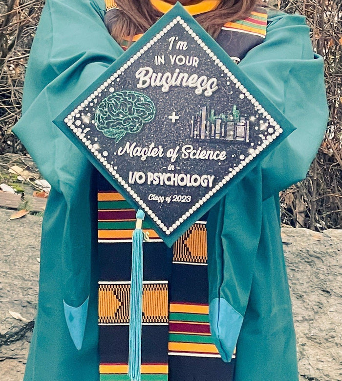 Graduate holding Im In Your Business IO Psychology cap