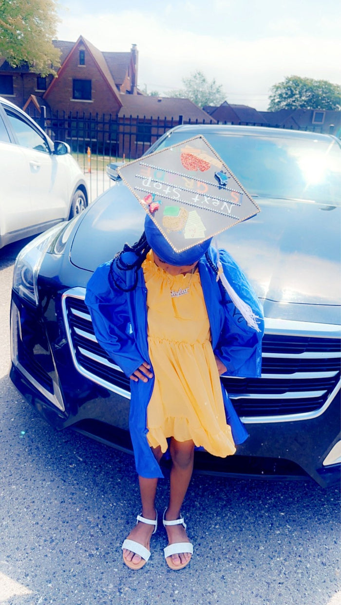 Young girl wearing Next Stop 2nd Grade cap by car