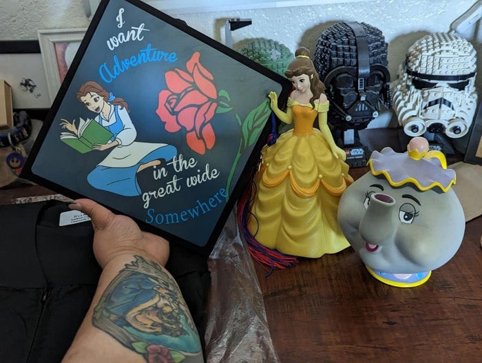 Tattooed arm holding Belle I Want Adventure topper